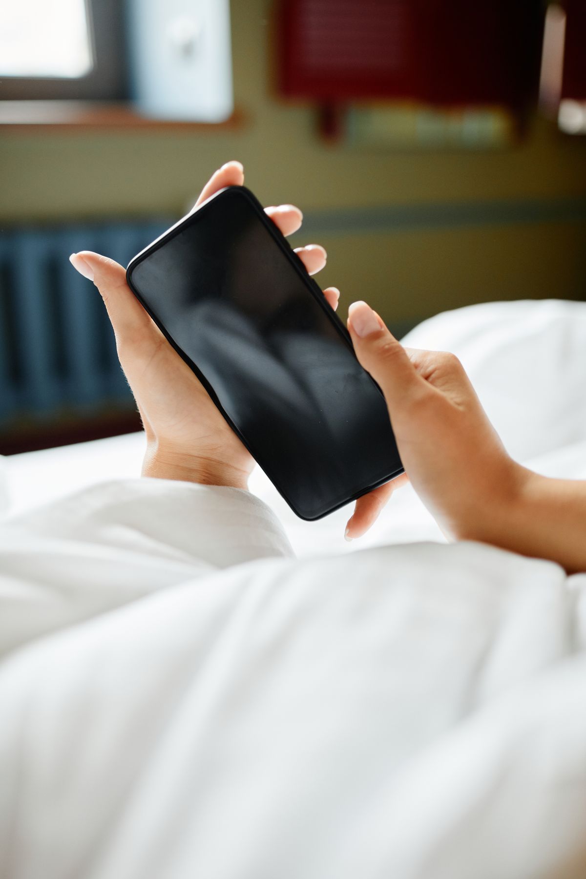 ベッドの上でスマホを両手で持っている様子（手元のみ）